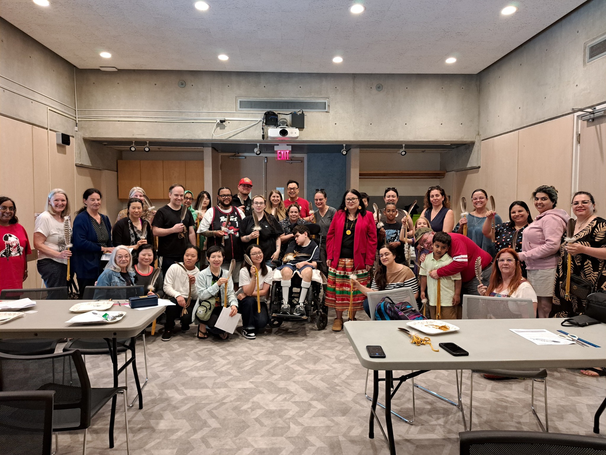 A large group of workshop participants holding up their completed smudge feathers after an Indigenous cultural session with Miskwaadesi Studio in Richmond Hill, Ontario.