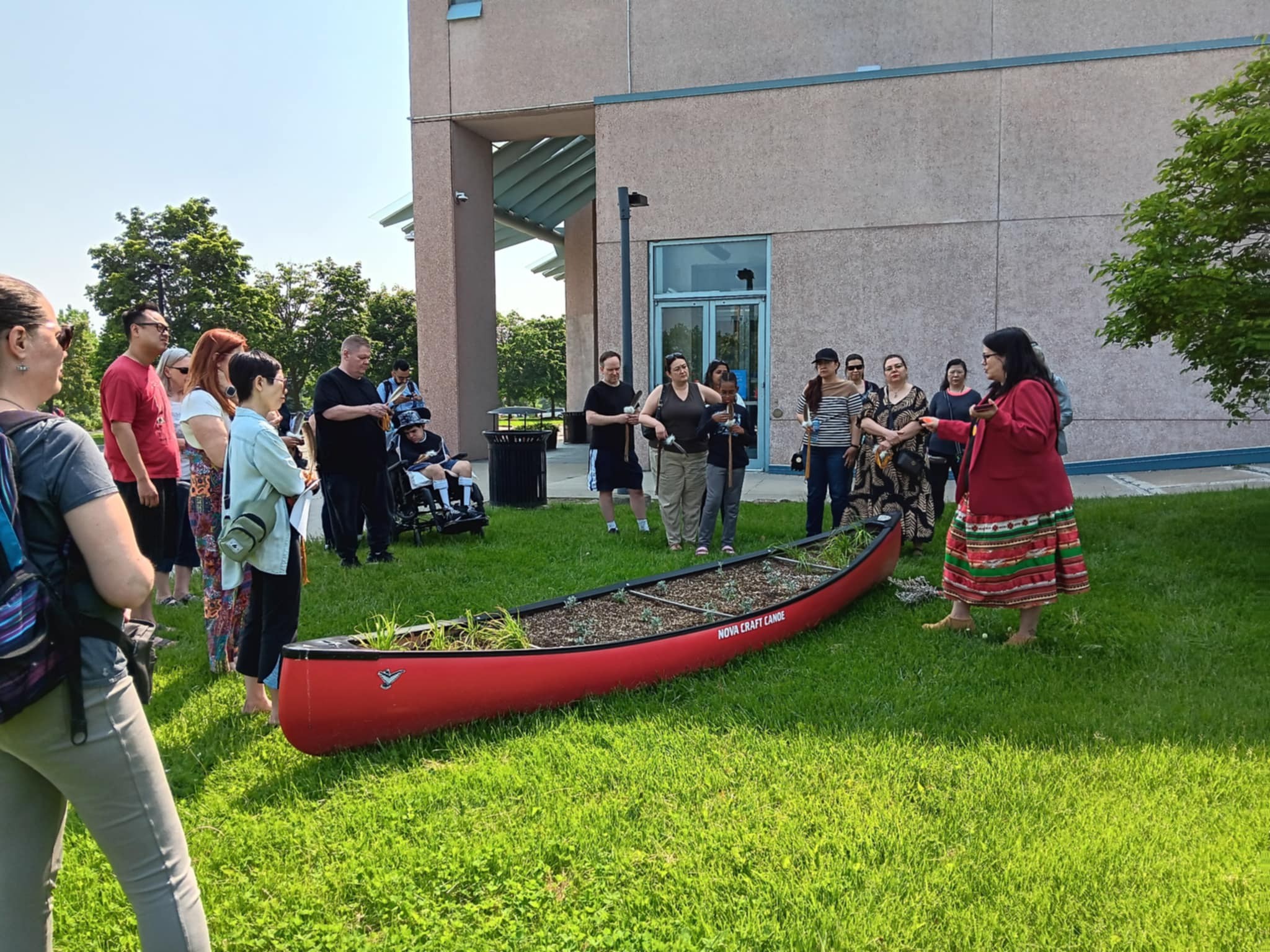 Participants of a smudge feather workshop standing around a red canoe medicine garden during a welcoming ceremony at Central Library in Richmond Hill, Ontario